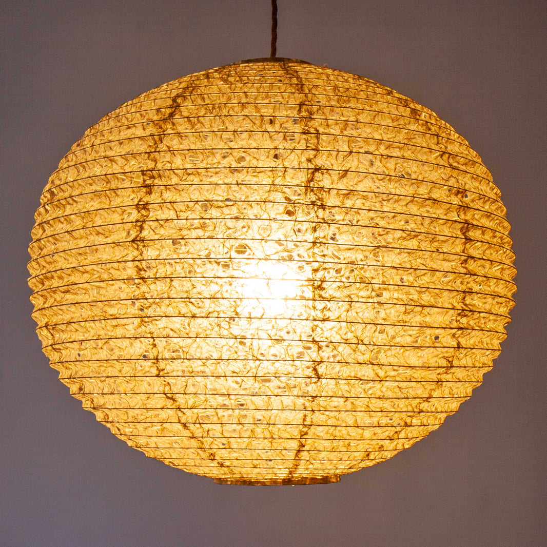 A large 53cm green/brown hemp washi paper lamp shade with small holes, hanging and casting a warm light.
