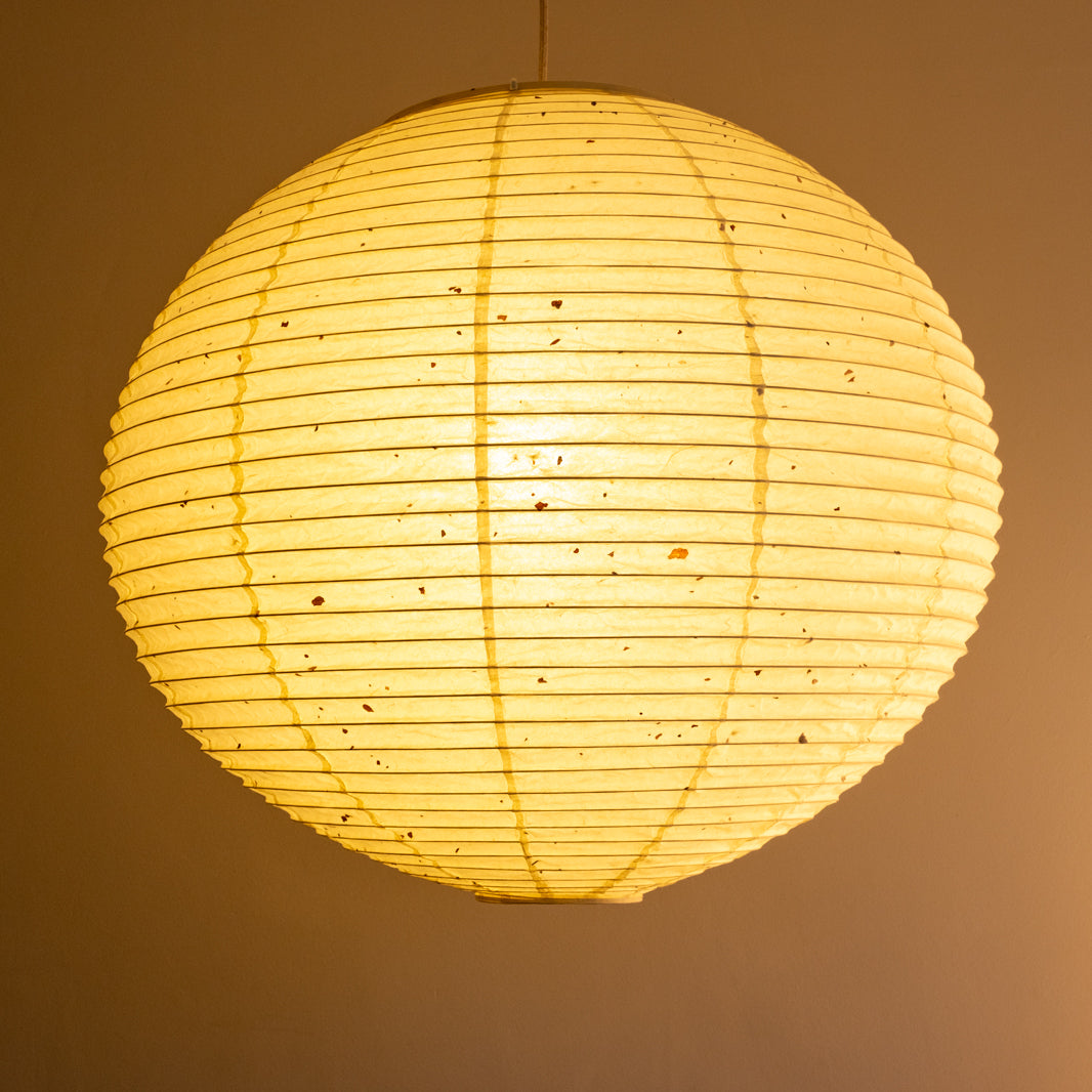 A 71cm, round, handmade kozo washi paper lamp shade with natural flecks, illuminated, side view